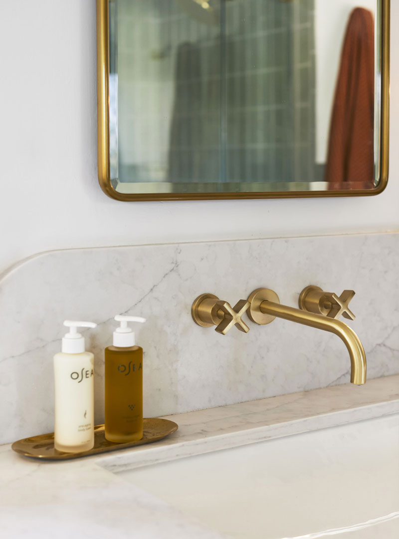 This image shows a quartz bathroom countertop attached to a white sink with gold hardware. Above the sink is a rectangular mirror with a gold border. Hand soap and hand lotion sit on the counter next to the sink. 