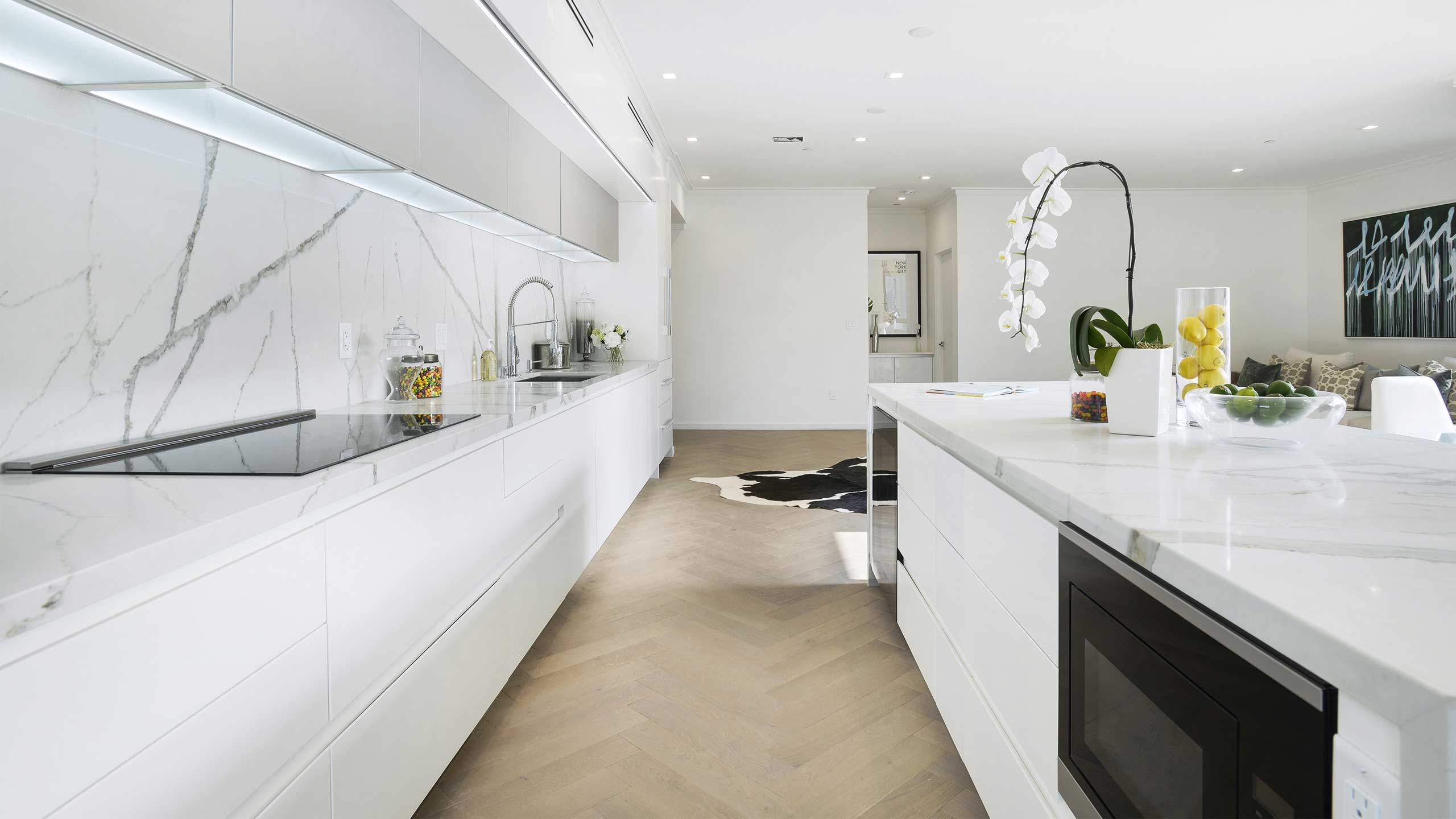 This kitchen has white cabinets and a white quartz countertop with fruit and flowers sitting on top.