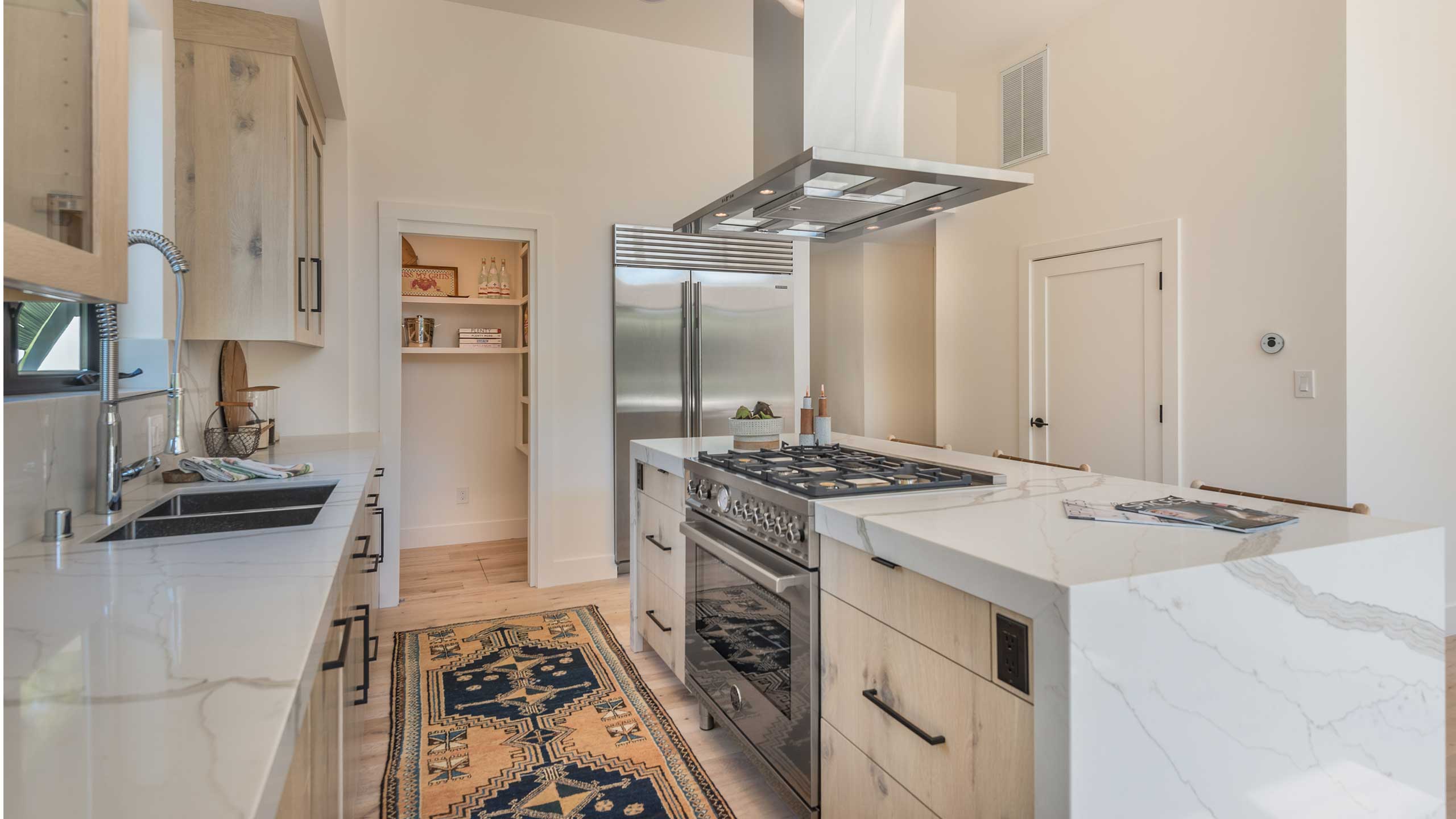 A kitchen featuring a white quartz countertop with veins and a large stovetop with a hanging fume hood is pictured.